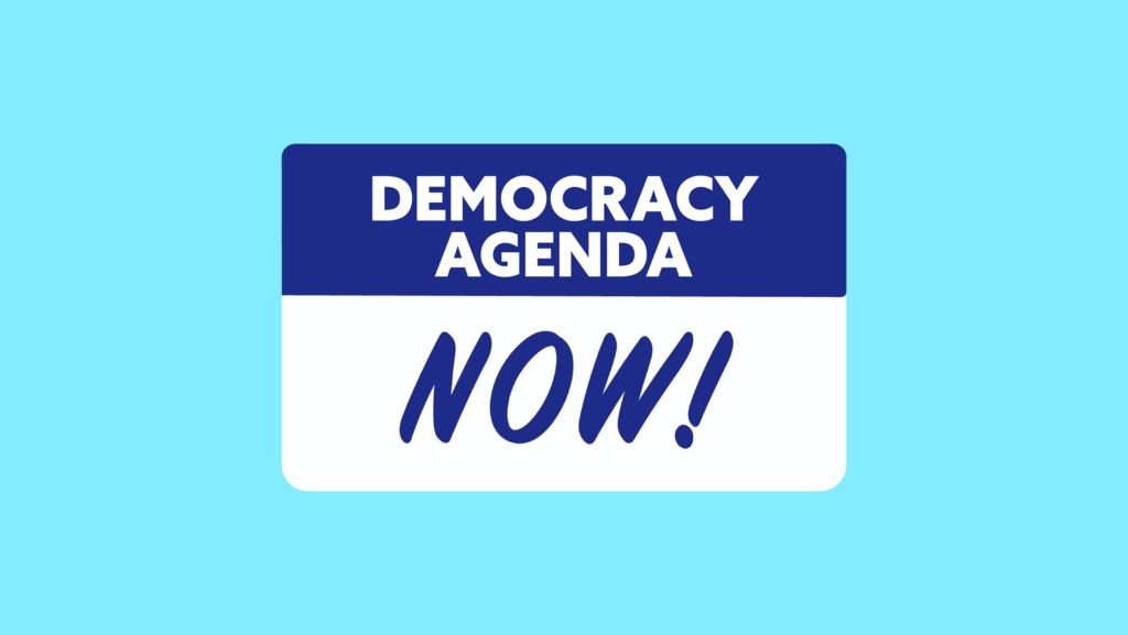 A blue and white protest sign that says "Democracy Agenda NOW!"