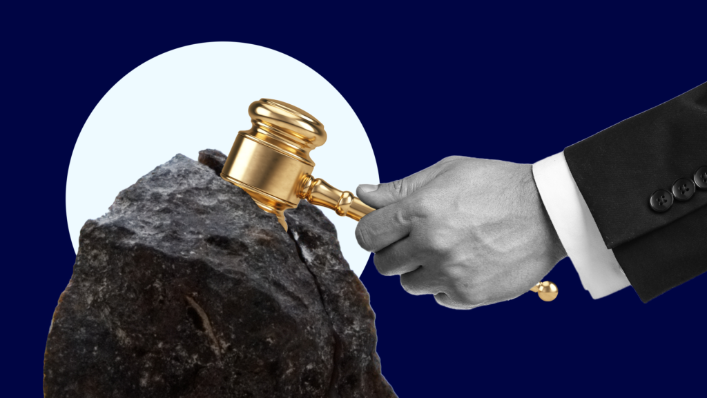 A male lawyer's hand attempting to remove a gold gavel lodged inside a black boulder