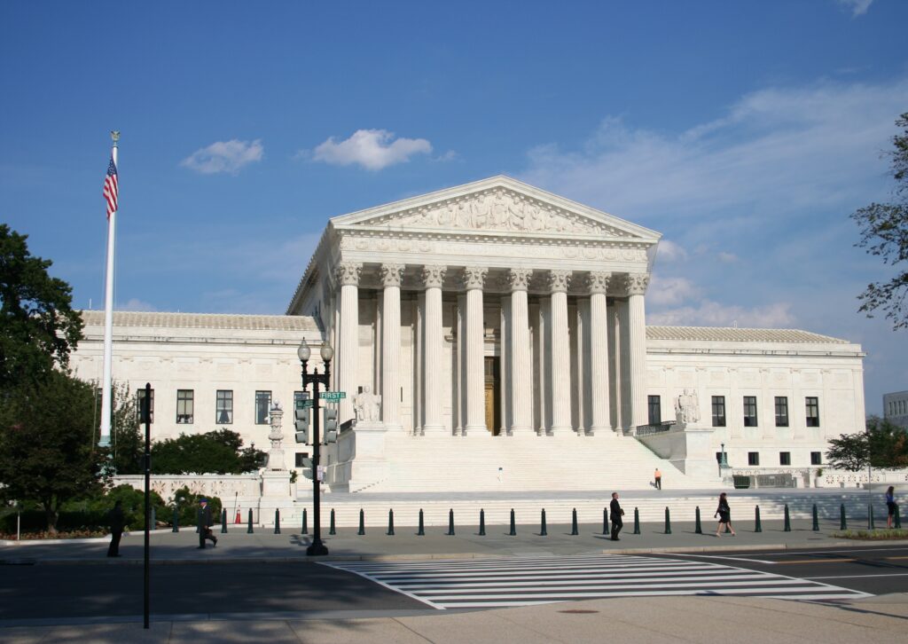 Photograph of U.S. Supreme Court in Washington D.C. The photograph features the U.S. Supreme Court in the center with the blue sky above the Court. (Adobe Stock) 