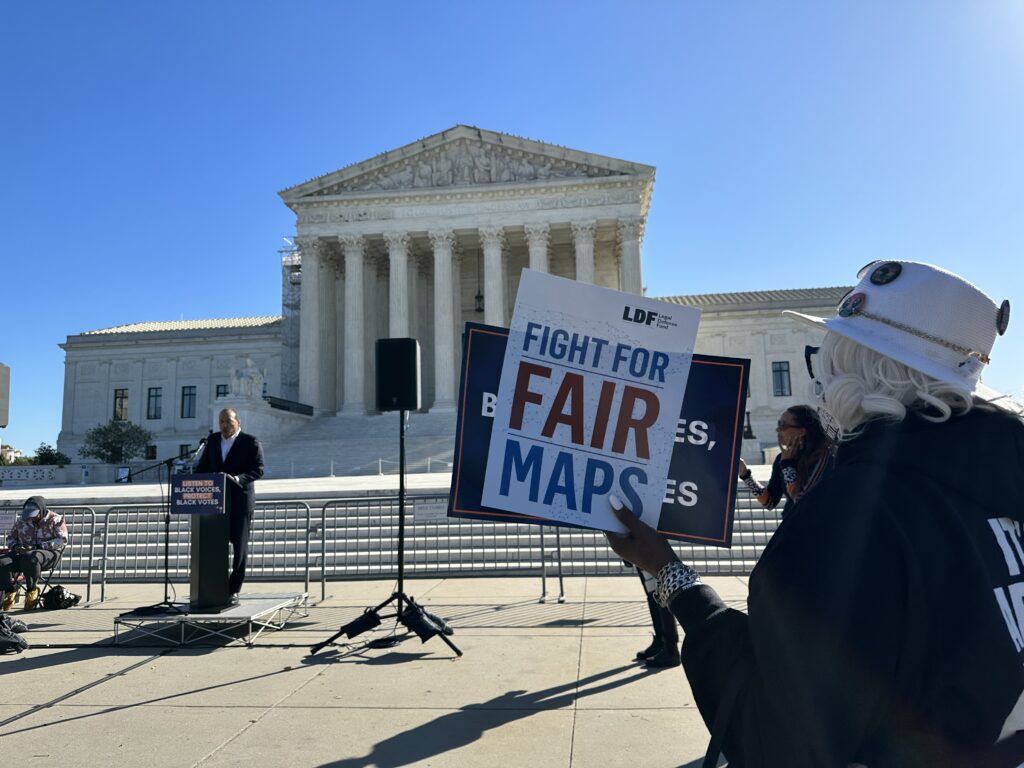 Picture of the U.S. Supreme Court featuring a person holding a sign that says "Fight For Fair Maps" in the foreground and Michael B. Moore, South Carolina advocate and Congressional candidate speaking