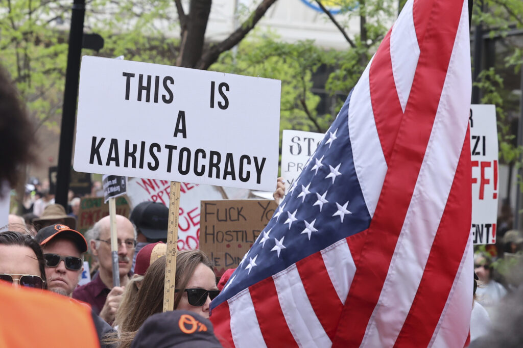 People holding signs while attending a rally against the Trump administration.