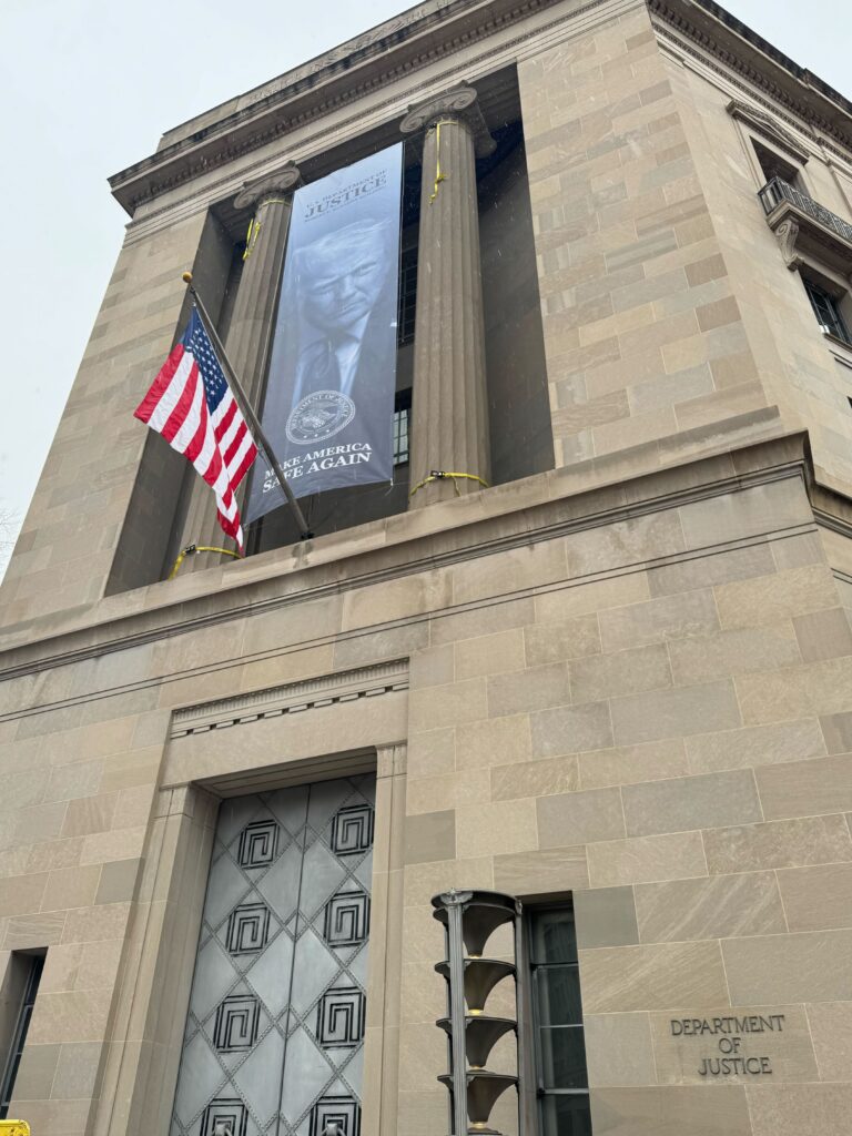 A banner with President Donald Trump's visage and 'Make America Great Again' campaign slogan is draped from the Department of Justice's main building in Washington, D.C. on Feb. 19, 2026 (Photo by Jacob Knutson/Democracy Docket)